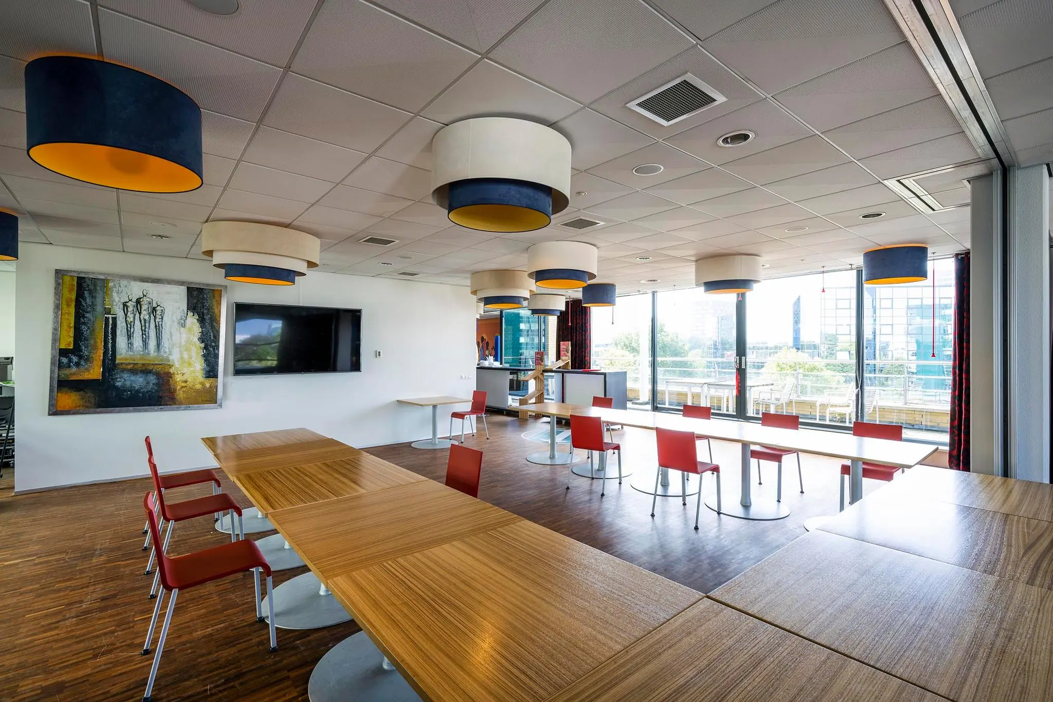 Moderne vergaderruimte aan de K.P. van der Mandelelaan met houten tafels, rode stoelen en grote ramen met uitzicht op kantoorgebouwen.